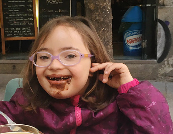 Una niña con gafas y con síndrome de Down aparece feliz con toda la boca manchada de chocolate.