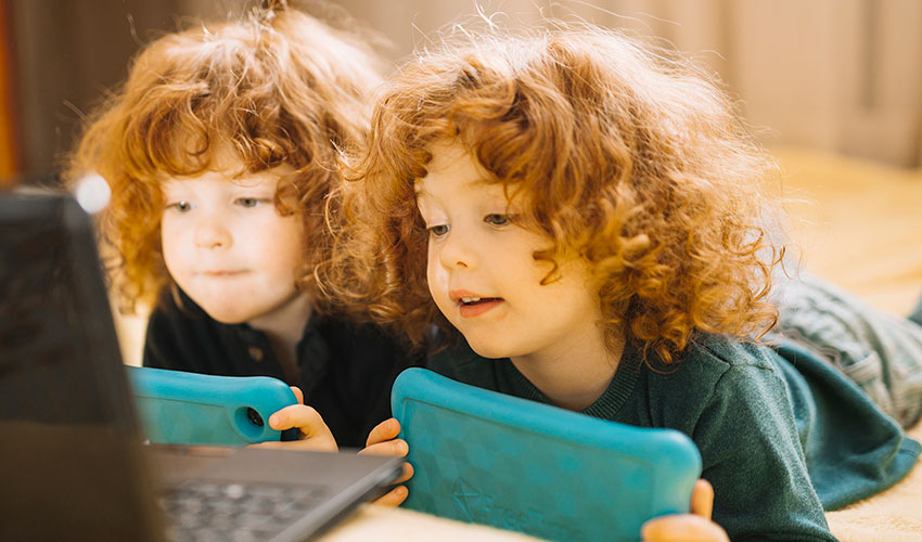 Imagen de unas niñas gemelas con tablet y frente al ordenador