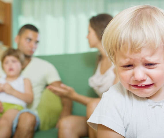 Imagen de un niño llorando con los padres discutiendo detras