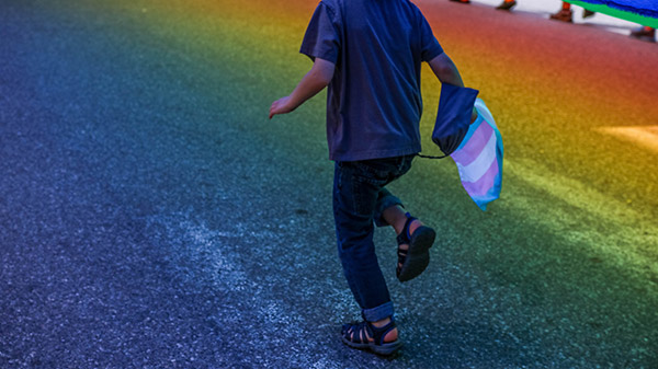 Niño corriendo sobre un suelo de color arcoiris y una bandera LGTBI