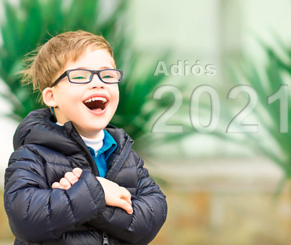 Niño con síndrome de Down con gafas y de aspecto sonriente con letras sobreimpresas en las que se lee: "Adiós 2021"