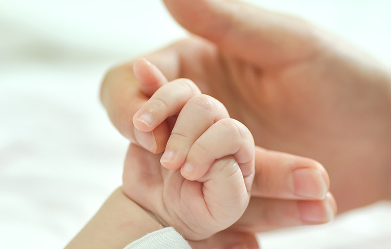 Mano de un bebé con síndrome de angelman cogiendo el dedo de su madre.