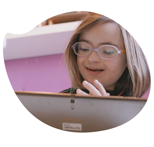 Una niña con síndrome de down está aprendiendo a leer y divirtiendose con una tablet.