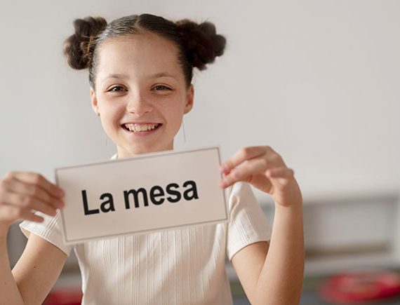Una niña muestra una targeta con la palabra "mesa" para aprender a leer con el método global de lectura.